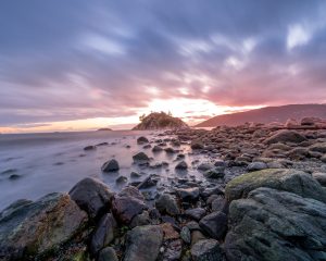 the sun is setting over a rocky beach